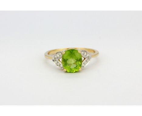 A 14ct yellow gold ring set with an oval cut peridot and diamond set shoulders, (N.5).
