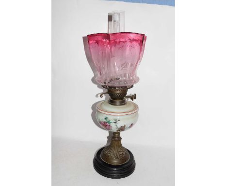 Victorian oil lamp with cranberry tinted glass shade over an opaque glass font and a brass column, 56cm high max