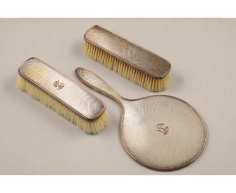George V two silver backed brushes and a matching hand mirror, machine turned decoration with a monogram in relief, assay mar