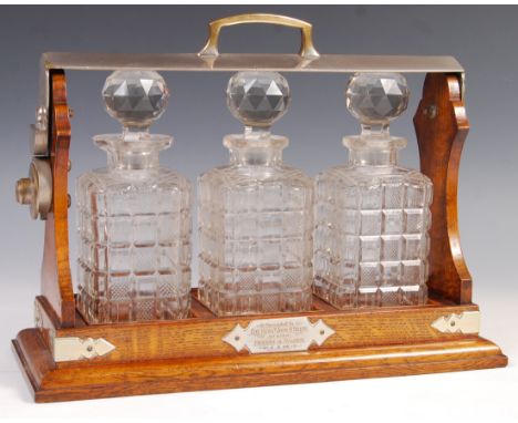 An antique early 20th century oak three-decanter tantalus. Oak construction, with gothic style silver plated adornments. Cont