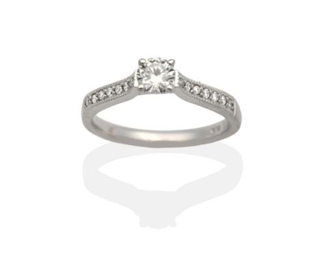 An 18 Carat White Gold Solitaire Diamond Ring, a round brilliant cut diamond in a claw setting, to diamond set shoulders, est