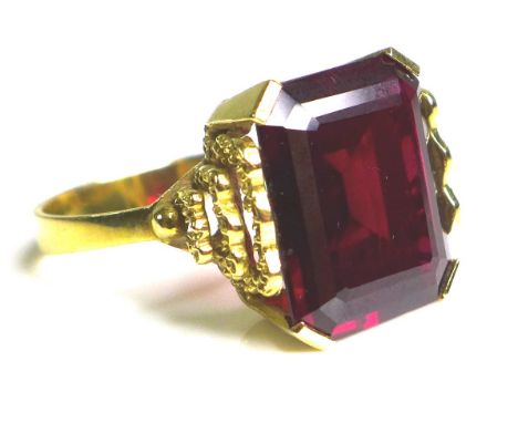 A Middle Eastern gold and imitation ruby dress ring, the emerald cut red stone, 40 by 20 by 5mm, in four claw setting with de