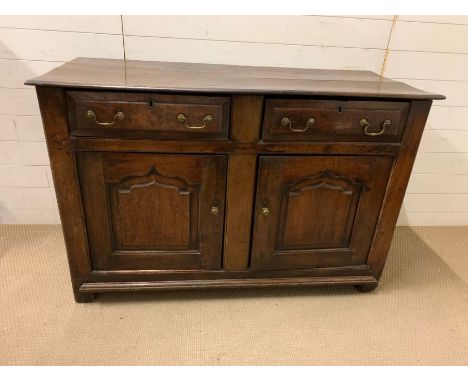 An oak side cupboard with two doors opening to a shelf and two drawers above, brass handles, panel sides and front on stile f