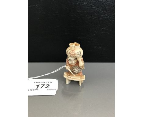 MEIJI PERIOD JAPANESE CARVED AND STAINED IVORY NETSUKE of a seated gentleman with a pot on his head, painted script