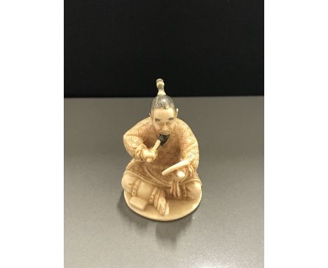 SUPERB QUALITY SIGNED JAPANESE IVORY NETSUKE, a seal pattern study of a Samurai seated in partial armour applying colour to h