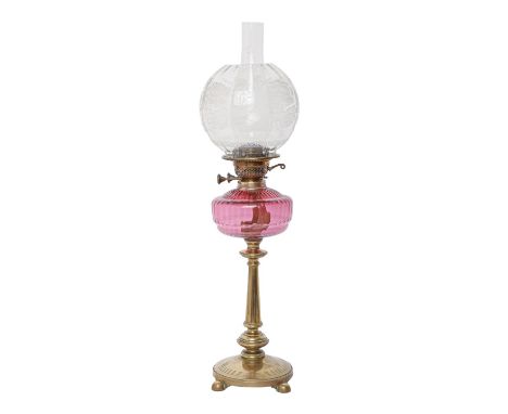 A brass oil lamp, c1900, on round base and four ball feet, moulded cranberry glass fount, brass burner, with etched shade, 62