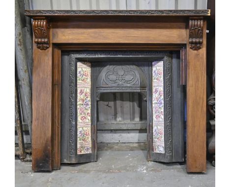 A carved and stained wood chimneypiece and a Victorian tiled cast iron hooded fire surround,&nbsp; chimneypiece 116cm h, 130c