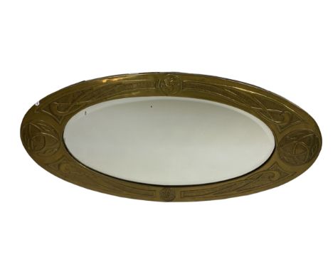 A Glasgow School Arts and Crafts brass mirror, the oval frame embossed with Celtic knot borders and roundels, with bevelled p