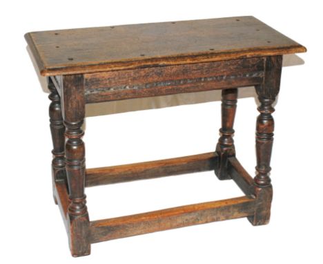 An 18th century oak joint stool of oblong form with shaped top, carving to the frieze, raised on turned legs with stretcher s