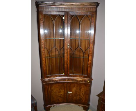 A reproduction mahogany inverted bowfront corner display cabinet, fitted a pair of glazed panel doors above solid panel doors