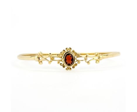 A 9ct yellow gold bangle set with an oval cut garnet, L. 6.5cm. Slightly bent.