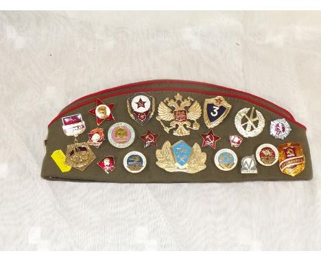 A Russian cap with three patch badges adhered and approximately 20 enamelled lapel and cap badges attached to the reverse.