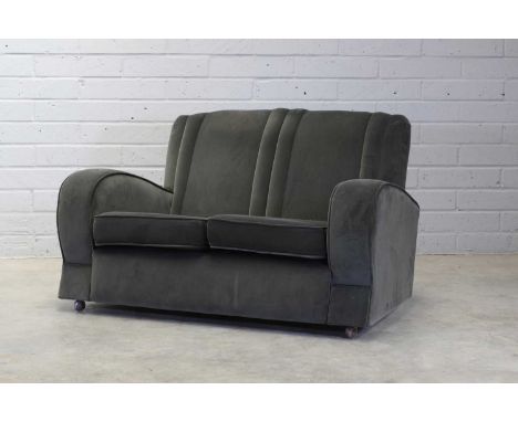An Art Deco club two-seater sofa,1930s, the moulded backrest over curved armrests, upholstered in grey velvet, on plastic cas