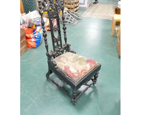 Heavily carved ebonised low chair with tapestry seat raised on castors