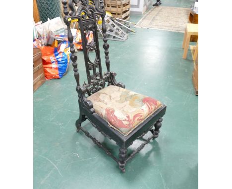 Heavily carved ebonised low chair with tapestry seat raised on castors