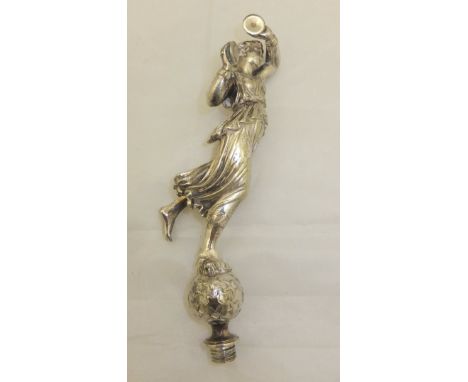 A white metal car mascot in the form of a maiden playing cymbals, raised on a ball of stars