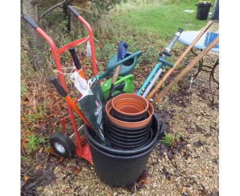A red painted sack truck, various long handled garden tools, plastic planters, two watering cans, etc