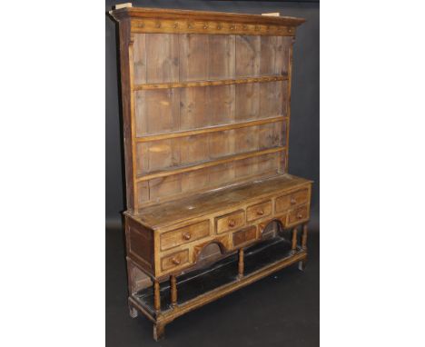 An 18th Century Welsh oak dresser, the boarded plate rack with stepped cornice above a set of cup hooks and three shelves ove