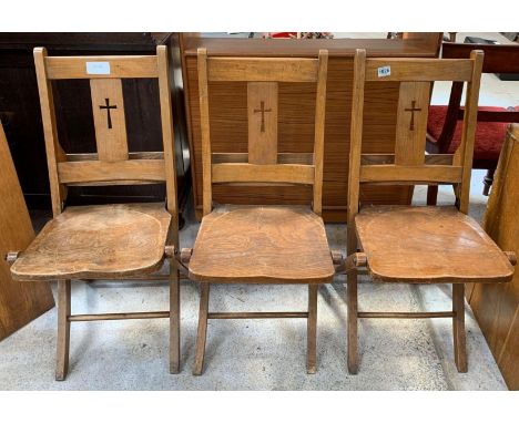 Three 20th century beech and oak folding church chairs, with cut out cross decoration to the back of each and shelf at back f