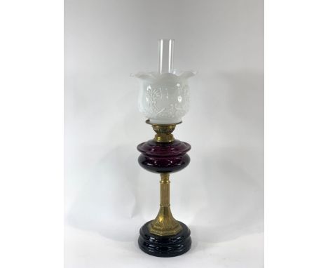 A Victorian oil lamp on black ceramic glazed base, with brass stem, dark purple glass reservoir, white opaque shade with embo