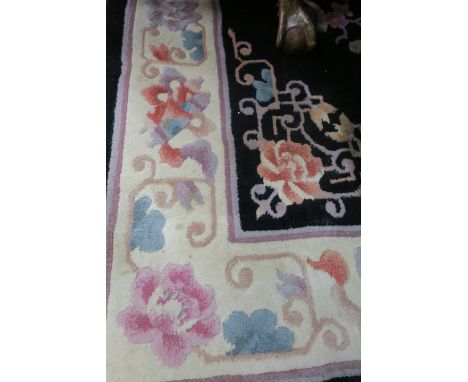 A RECTANGUALR WOOL RUG the black central panel decorated with Oriental style foliate motifs with a cream foliate filled borde