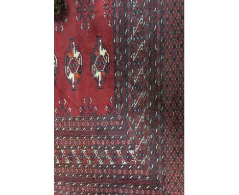 A RECTANGULAR BOKHARA RUG, the red ground with central panel filled with geometric patterns within graduation borders. 254cms