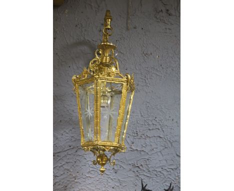 A PAIR OF GILT BRASS WALL LANTERNS, with scroll arms and engraved glass panels of octagonal outine with urn finial.