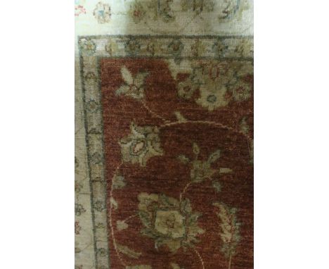 A RECTANGULAR WOOL RUG, the rust central panel decorated with foliate motifs with a gold border and white fringing
