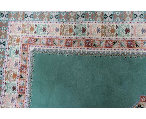 A RECTANGULAR WOOL RUG the central green ground panel decorated with a foliate motif with multiple borders and white fringing