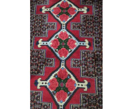 A PERSIAN SENNEH RUNNER, the central geometric shaped panel filled with pink flower heads flanked by foliate motifs with a gr
