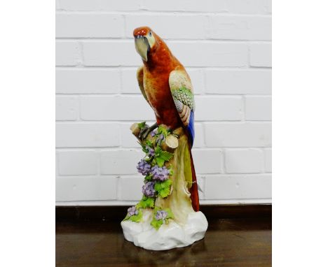 A porcelain figure of a parrot, model perched upon a tree stump on a naturalistic rocky base, has a gold anchor mark to the b