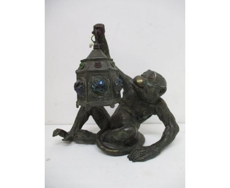 An early 20th century patinated spelter lamp fashioned as a seated monkey, holding a lantern with iridescent green and red gl