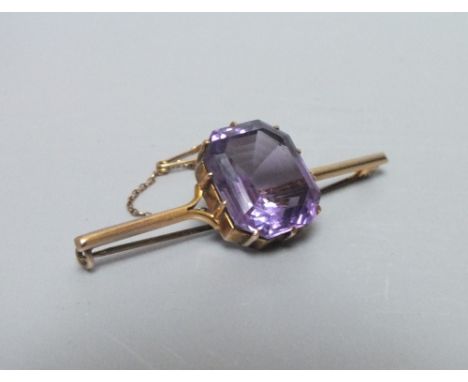 A YELLOW METAL AND AMETHYST BAR BROOCH, the large central emerald cut stone approximately 1.9 x 1.6 cm, overall L 5.5 cm