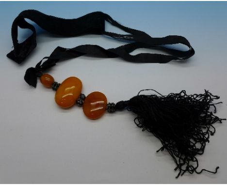 Three butterscotch amber beads and black silk sash, largest bead 37mm x 25mm