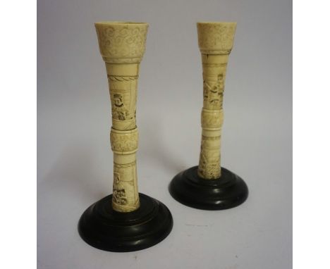 A Pair of Japanese Ivory Candlesticks, Meiji Period, Decorated with carved panels of figures, raised on an ebonised circular 