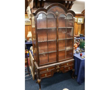 A walnut china cabinet on stand, the triple arch top above a pair of astragal glazed doors upon stand with assortment of five