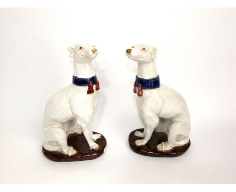 A pair of large ceramic models of seated hounds in the 19th century manner, both wearing tasselled blue collars and raised on