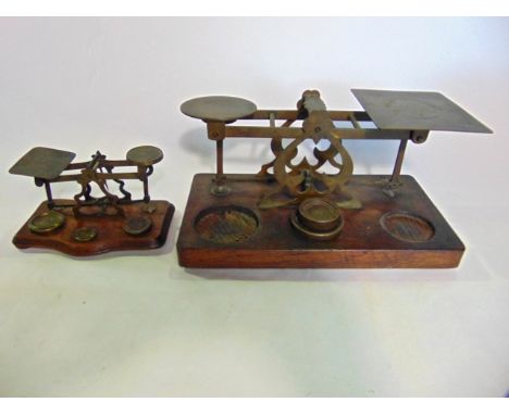Two vintage brass postal scales of varying size, both raised on wooden platform bases
