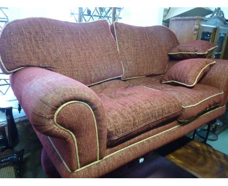 A substantial two seat sofa with scrolled arms and shaped back with deep red upholstered finish