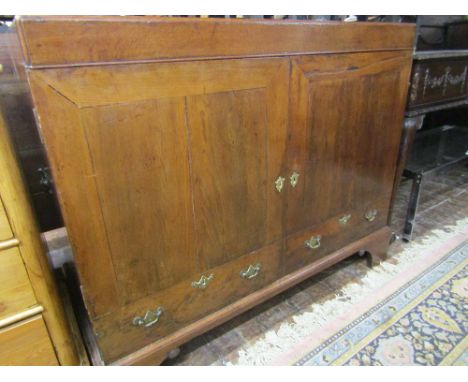 A Georgian yew wood cabinet, the front elevation enclosed by two panelled doors and two dummy drawers raised on bracket suppo