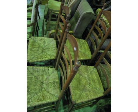 A set of four Edwardian oak ladder-back dining chairs with turned finials with rush seats on turned supports and stretchers