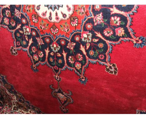 A red ground Persian style wool carpet, the central field with shaped medallion within an alternating cream and blue running 