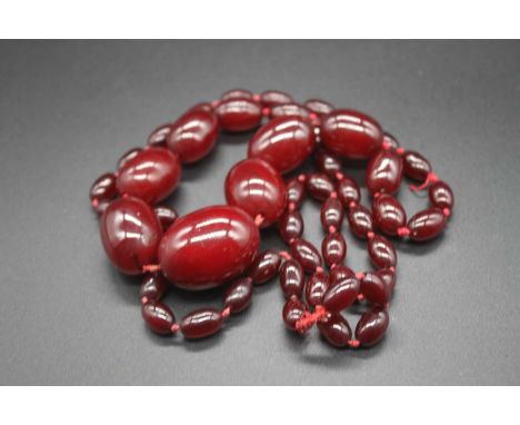 A cherry amber single string necklace, the graduated oval barrel beads on a knotted string, the largest bead measuring approx