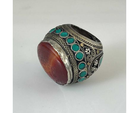 A large Islamic ring of bulbous form, 19th Century, the wrought metalwork inlaid with turquoise stones and with the face a la