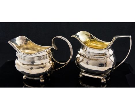 Two George III silver cream jugs, Neoclassical helmet form, on ball feet, gadrooned borders and strap handles, London 1811, 1