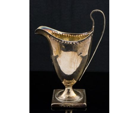 A George III silver cream jug, pedestal Neoclassical helmet form, on square base, repousse beaded border, London 1794, 14cm h