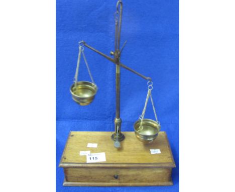 Set of brass and steel balance scales with brass bowl shaped pans on a wooden drawer base.