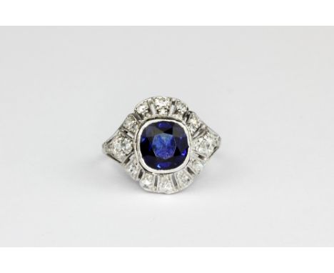 A white metal (tested high carat gold) ring set with a cushion cut sapphire surrounded by cut diamonds, (N.5).