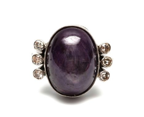 14 kt. Witgouden ring, bezet met een ovale sterrobijn (14,5 x 11 mm), met aan weerszijden drie achtkant geslepen diamanten me