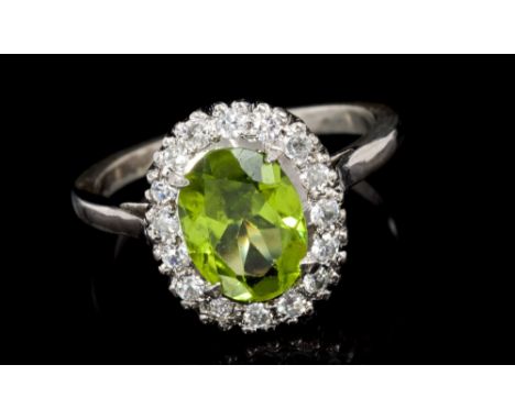 Peridot and diamond cluster ring, centred with an oval mixed cut peridot surrounded by sixteen brilliant cut diamonds with pi